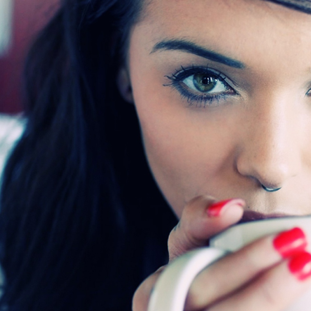 Девушка брюнетка с пирсингом в носу и красными ногтями