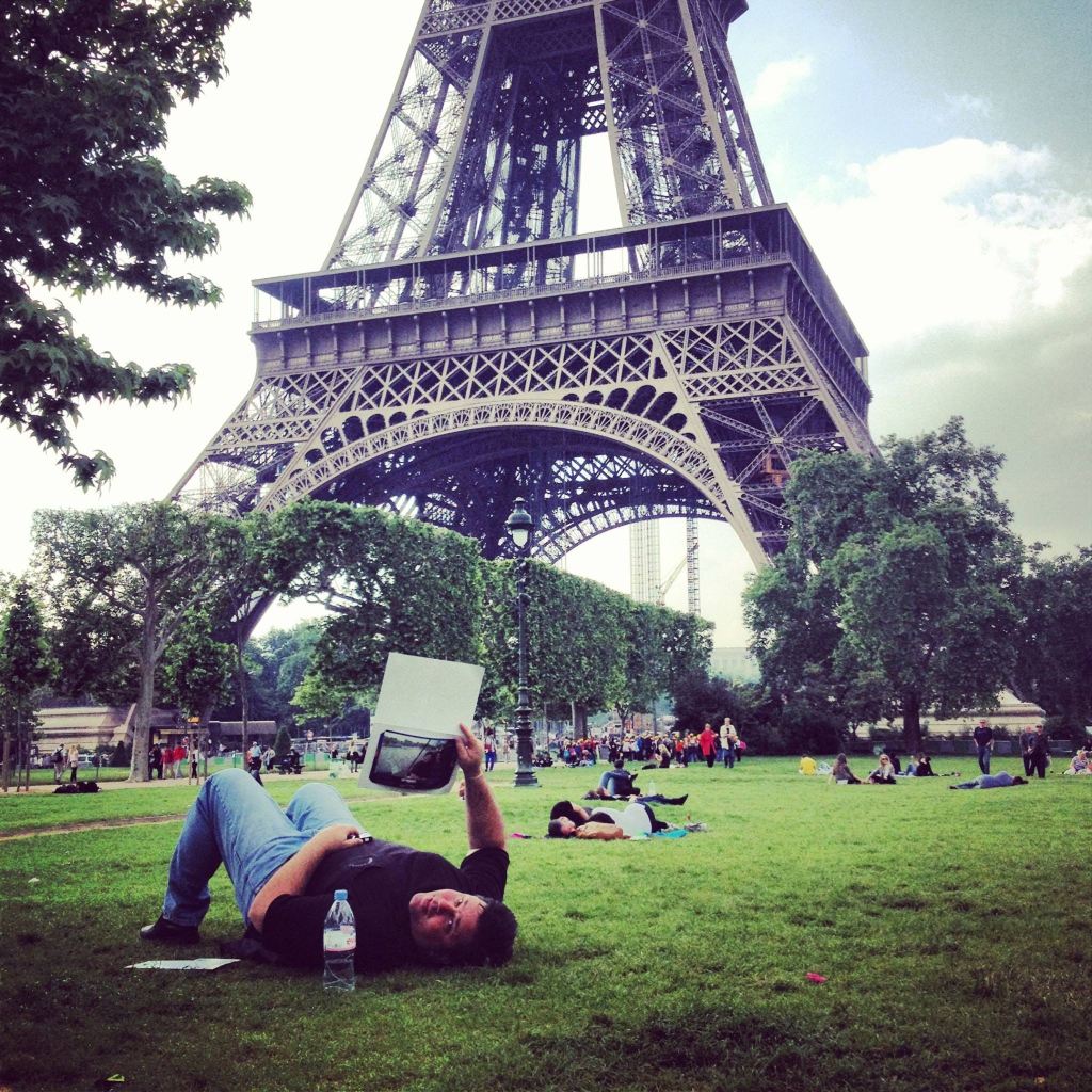 Люди отдыхают на траве возле Эйфелевой башни