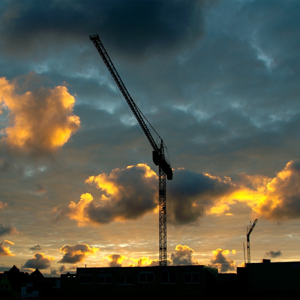 Стрелы кранов на стройке на фоне облаков