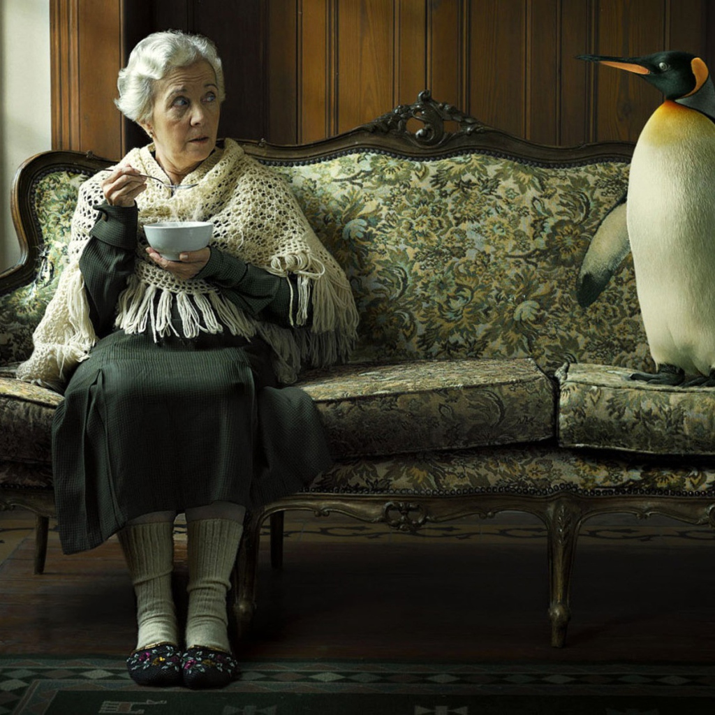 Пожилая женщина кушает суп и смотрит на пингвина