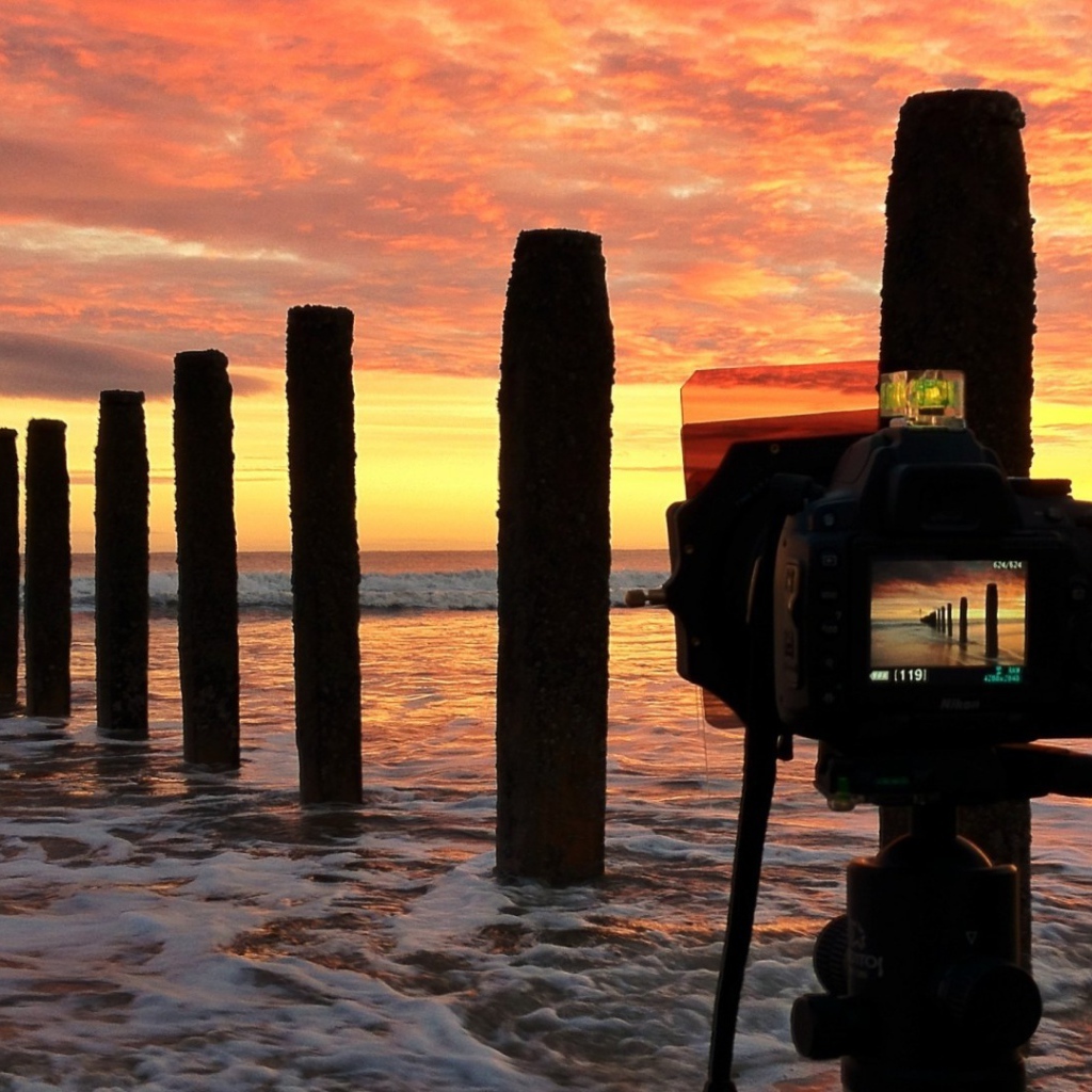 Фотограф снимает закат на берегу моря