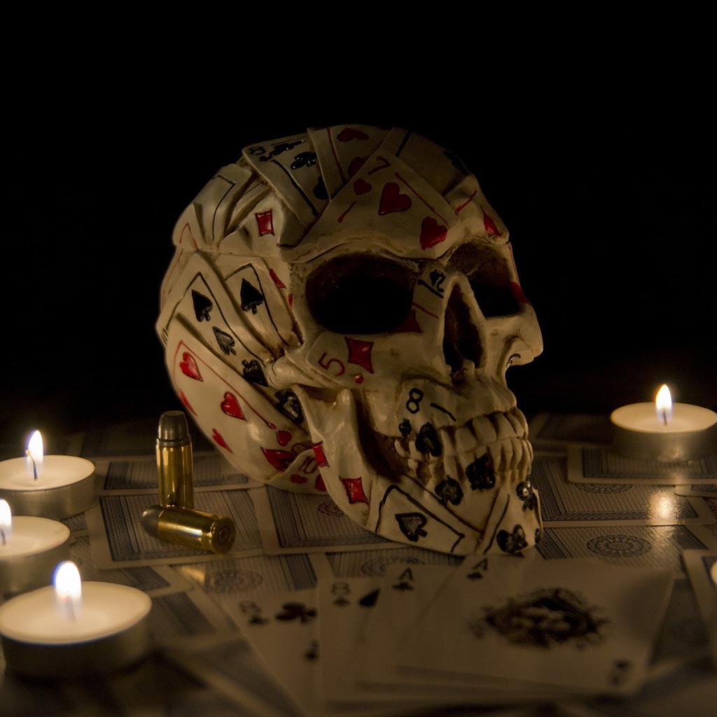 Череп из игровых карт среди свечей
