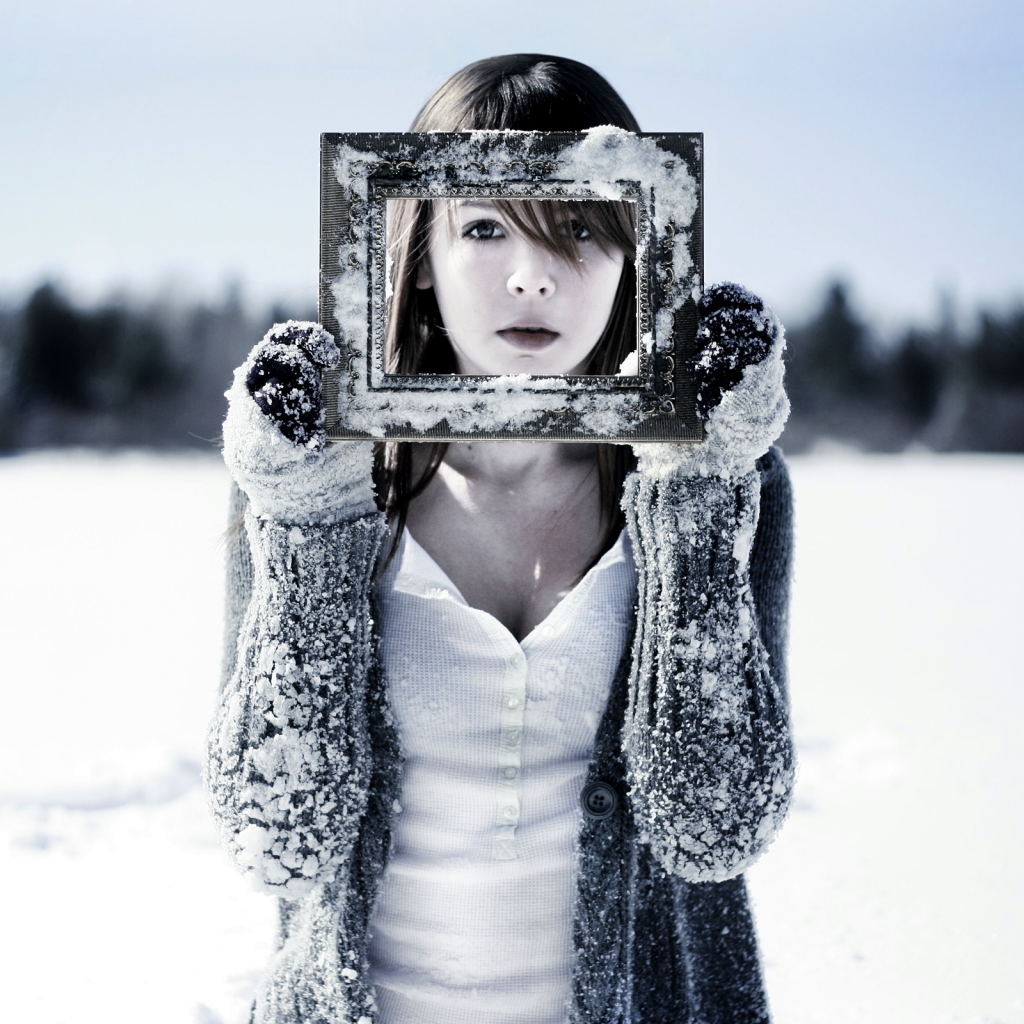 Девушка держит в руках фоторамку в снегу