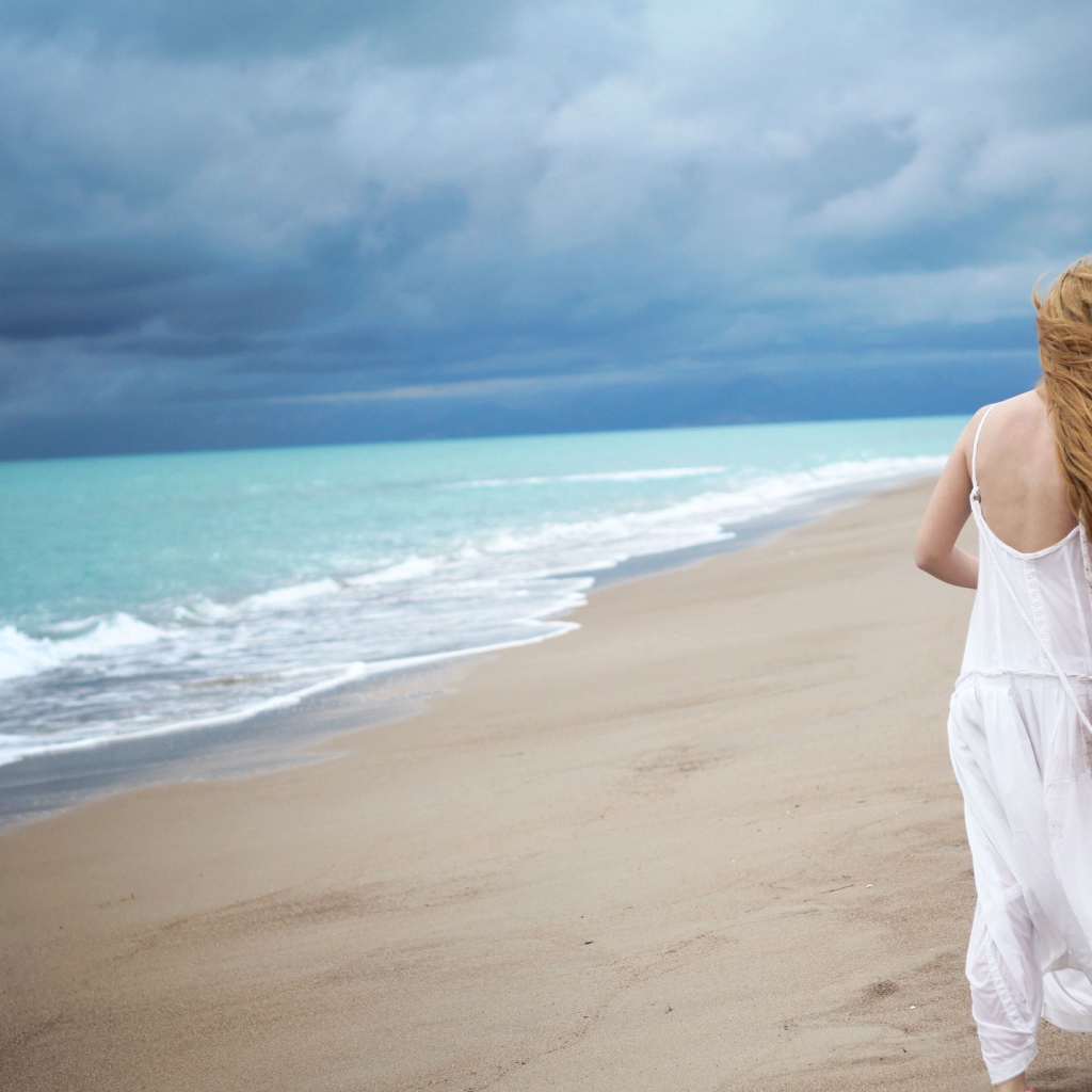 Девушка в белом платье идет по пляжу