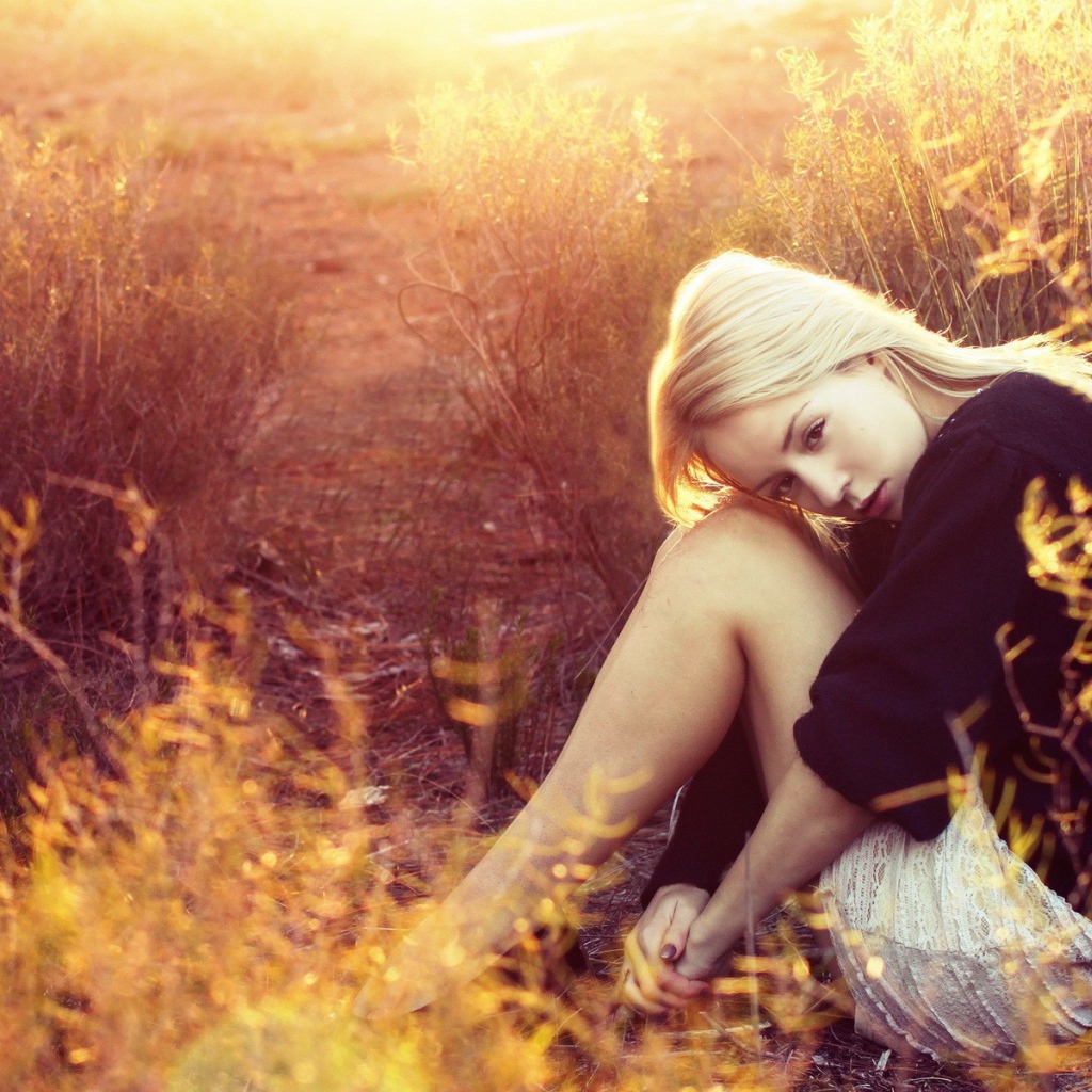 Блондинка сидит среди кустарников