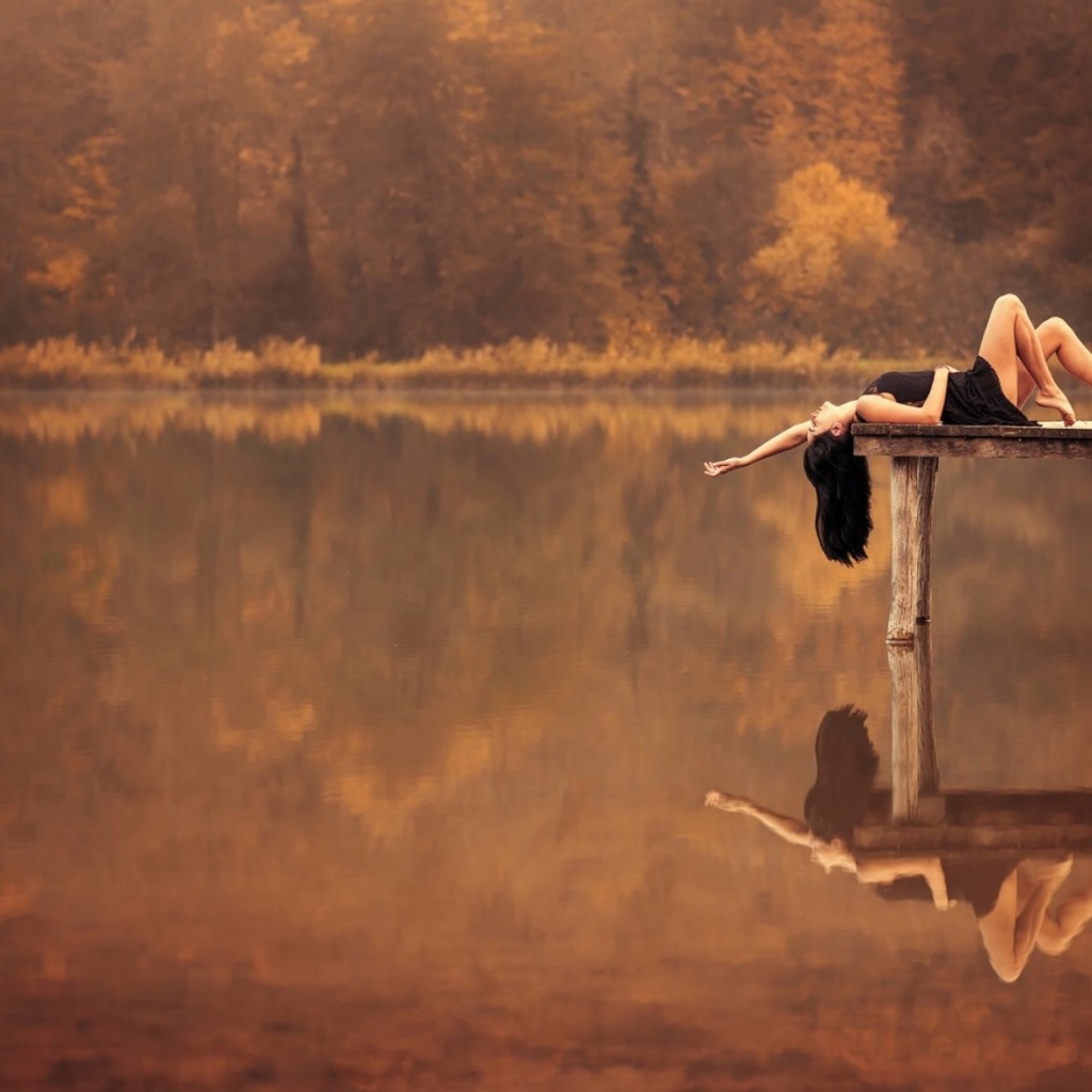 Брюнетка лежит на пирсе на озере