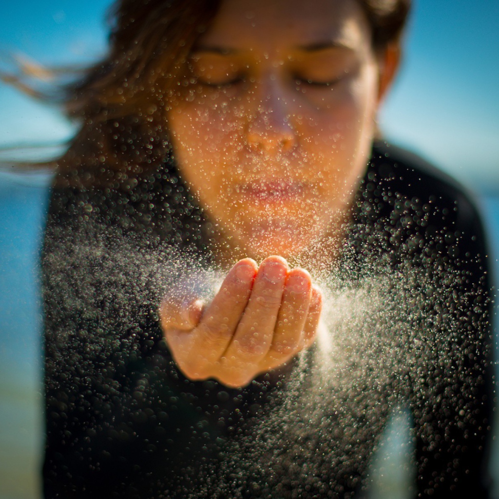 Девушка сдувает песок с руки