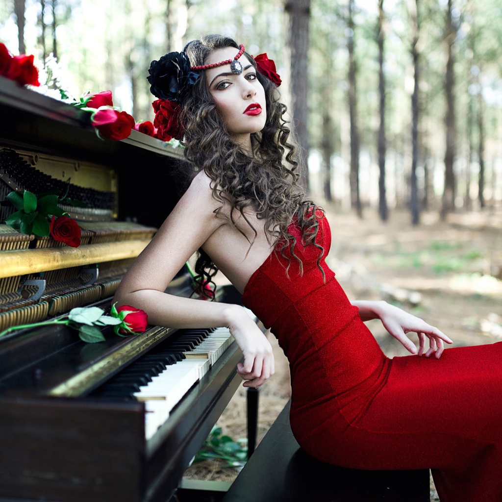 Девушка в красном платье сидит у пианино
