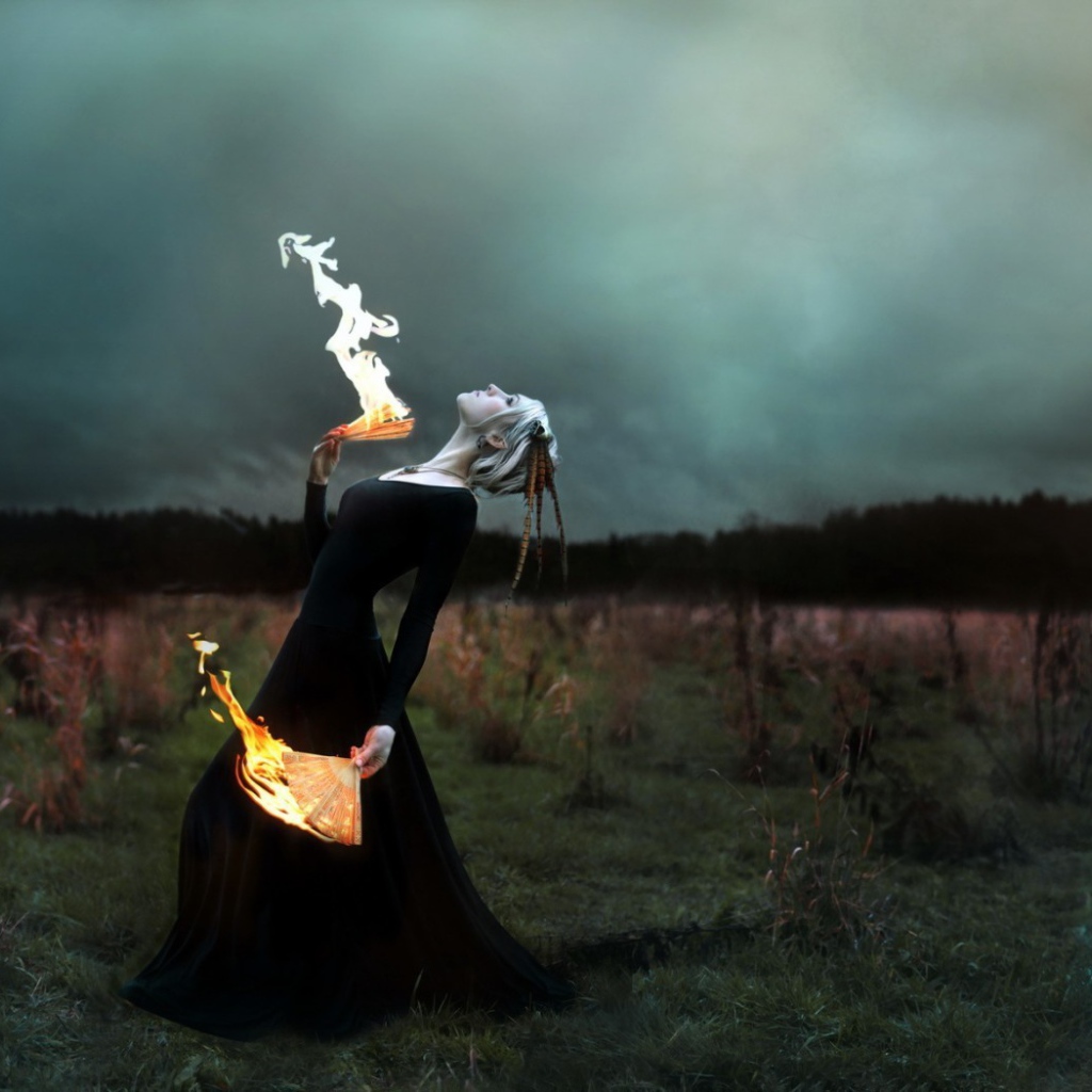 Девушка в черном платье играет с огнем
