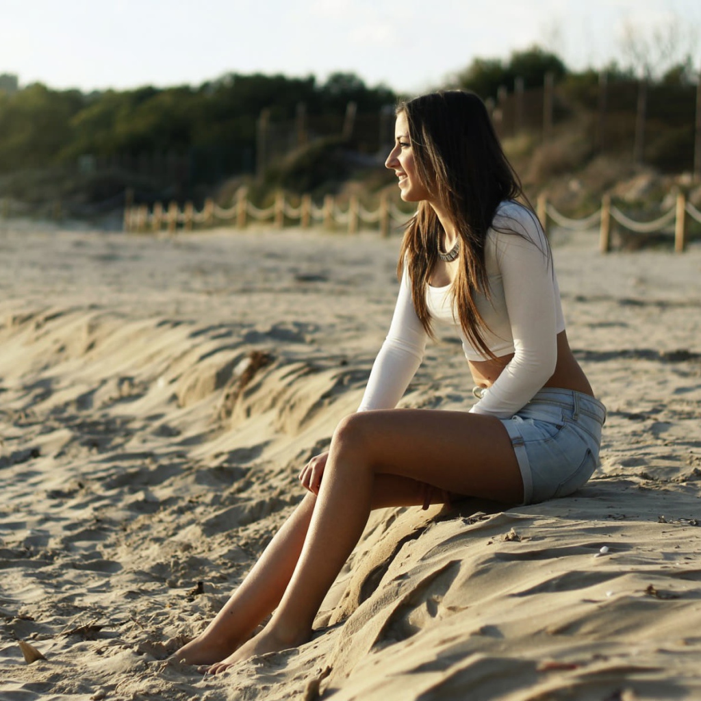 Девушка в джинсовых шортах сидит на песке пляжа