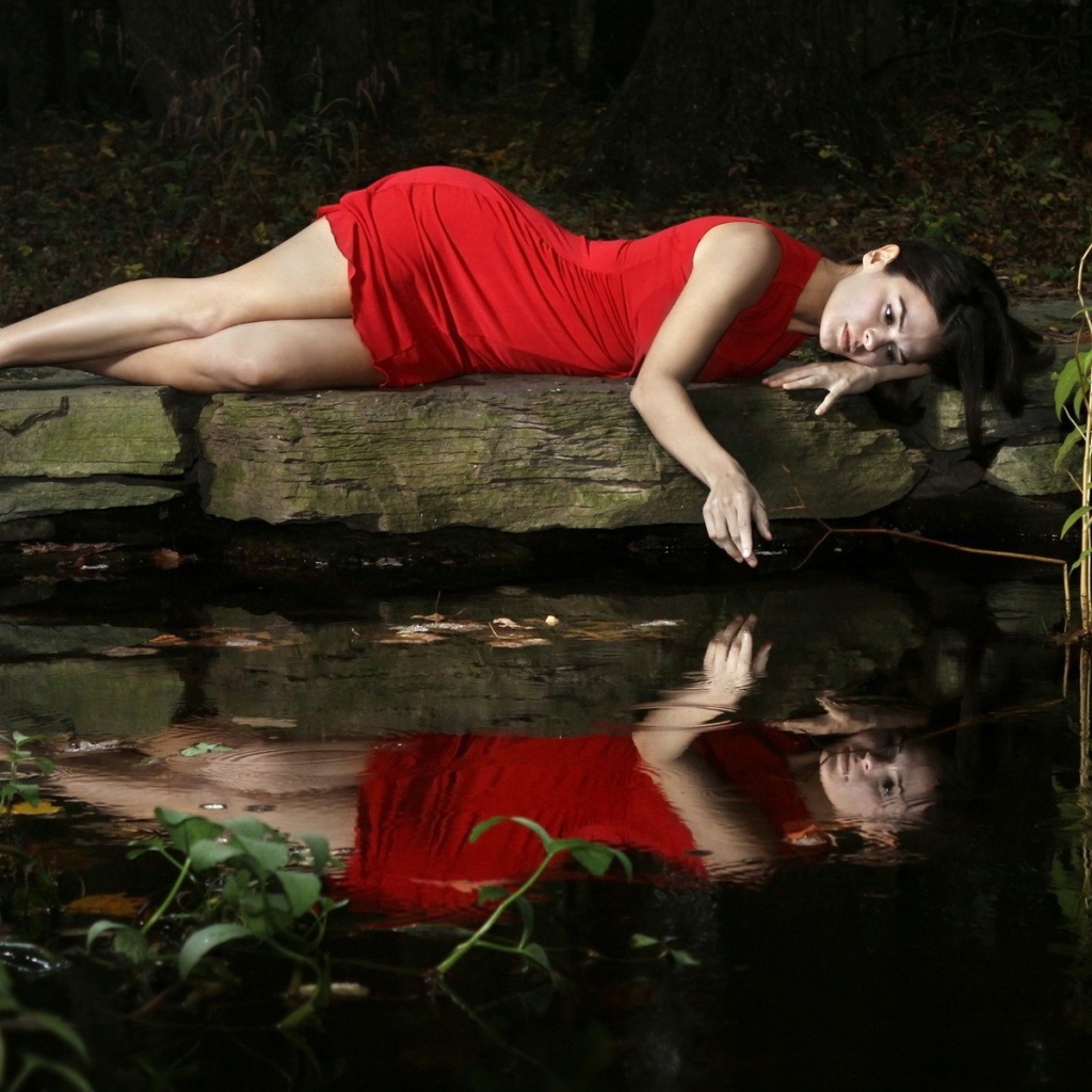Девушка в красном платье лежит на камне у водоема