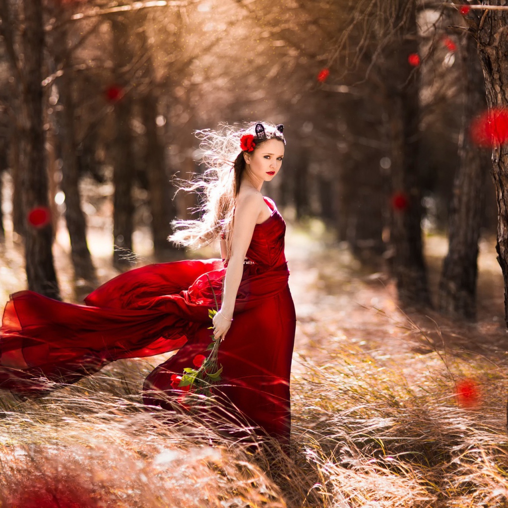Девушка в красном платье стоит в ветренном лесу