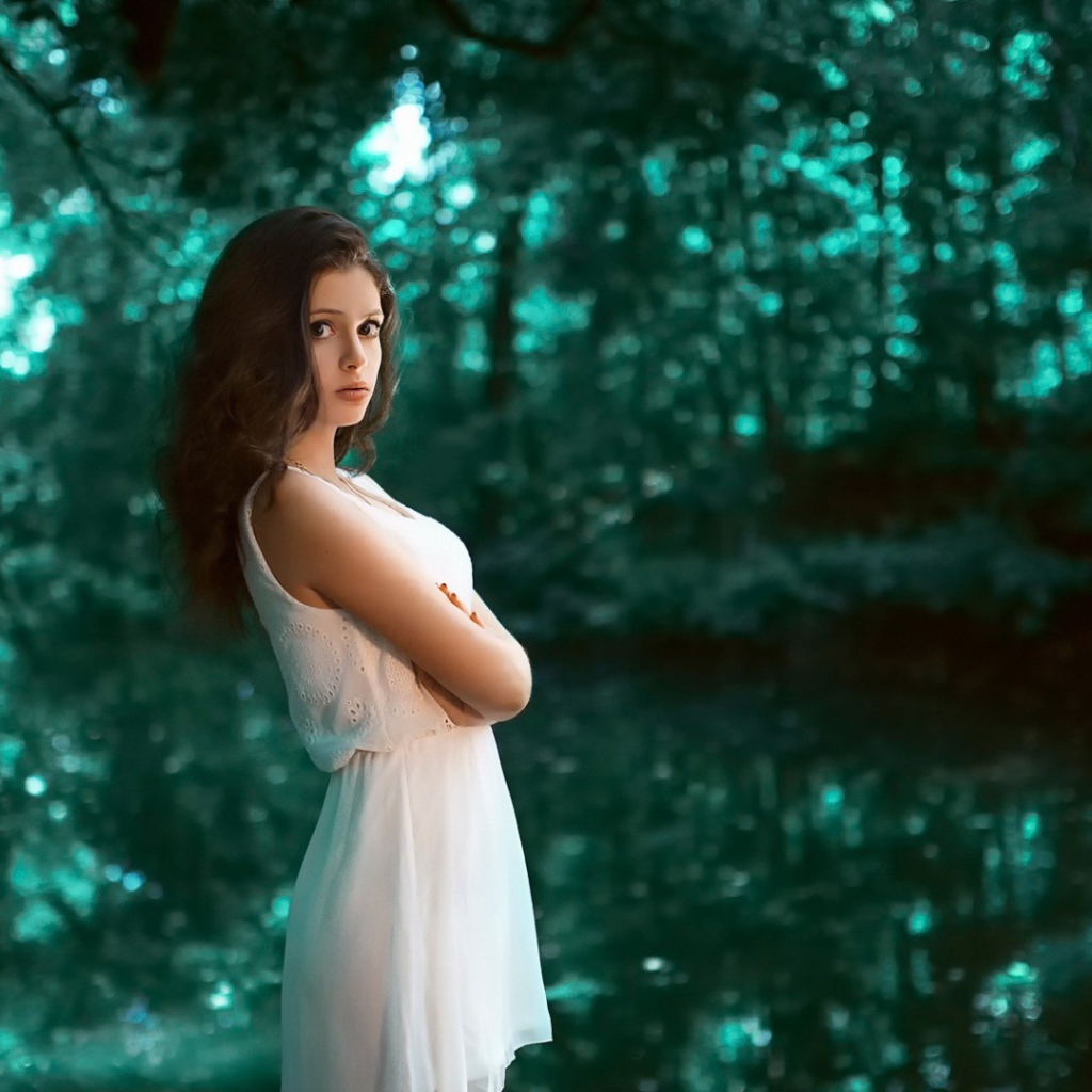 Девушка в белом платье стоит в зеленом лесу