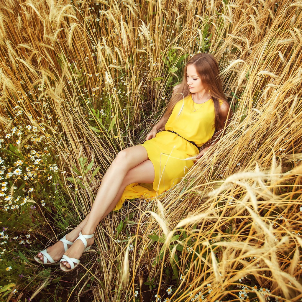Девушка в желтом платье лежит на колосках пшеницы