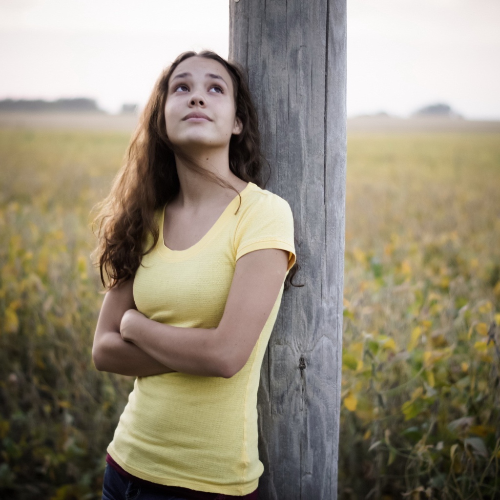 Девушка в желтой майке стоит у столба