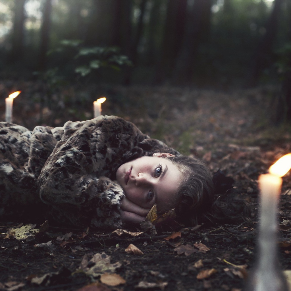Девушка лежит среди свечей в лесу