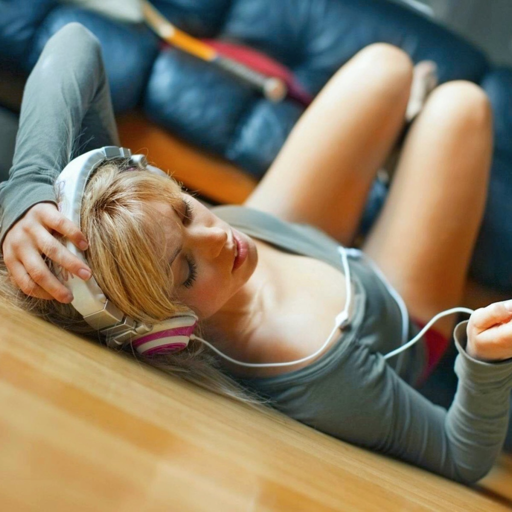 Девушка лежит на паркете и слушает музыку в наушниках