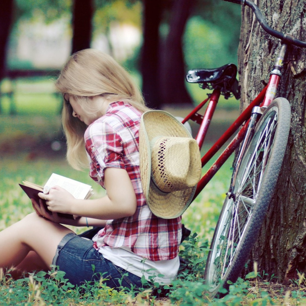 Девушка читает книгу сидя в парке на газоне