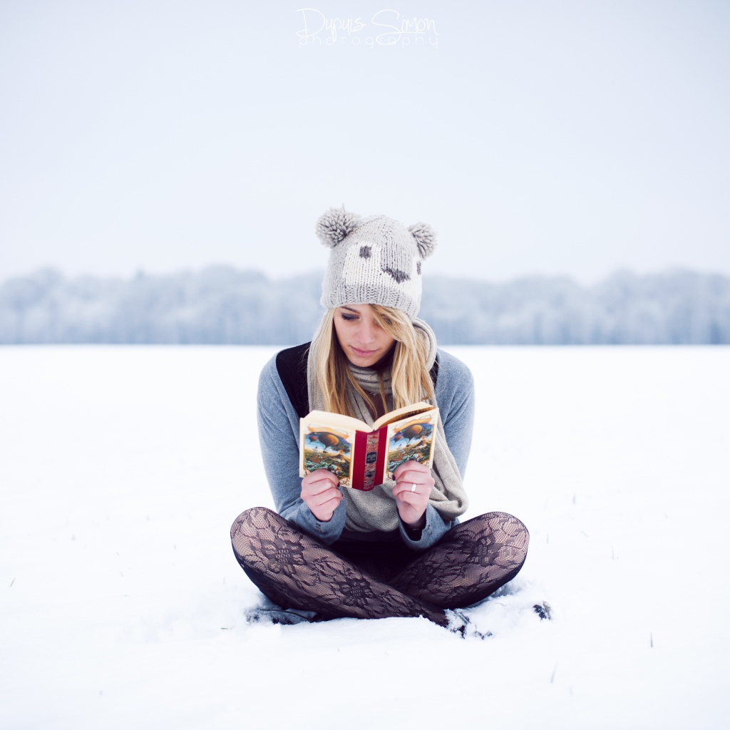 Девушка читает книгу сидя на снегу