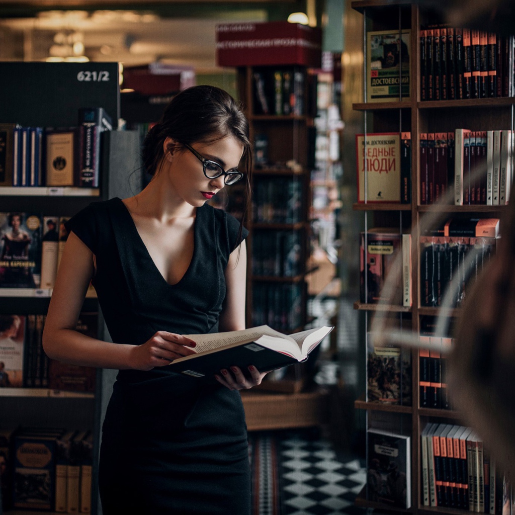 Девушка читает среди книжных полок