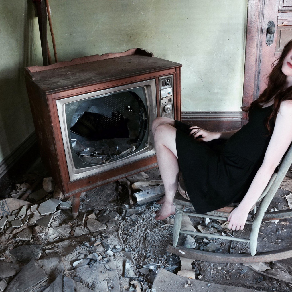 Девушка сидит у разбитого старого телевизора