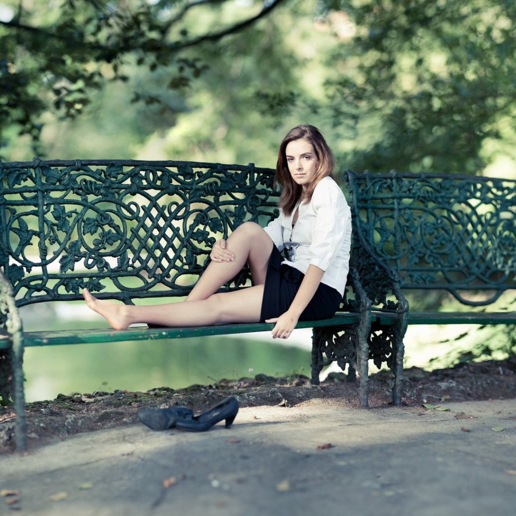 Девушка сидит на кованной парковой скамье