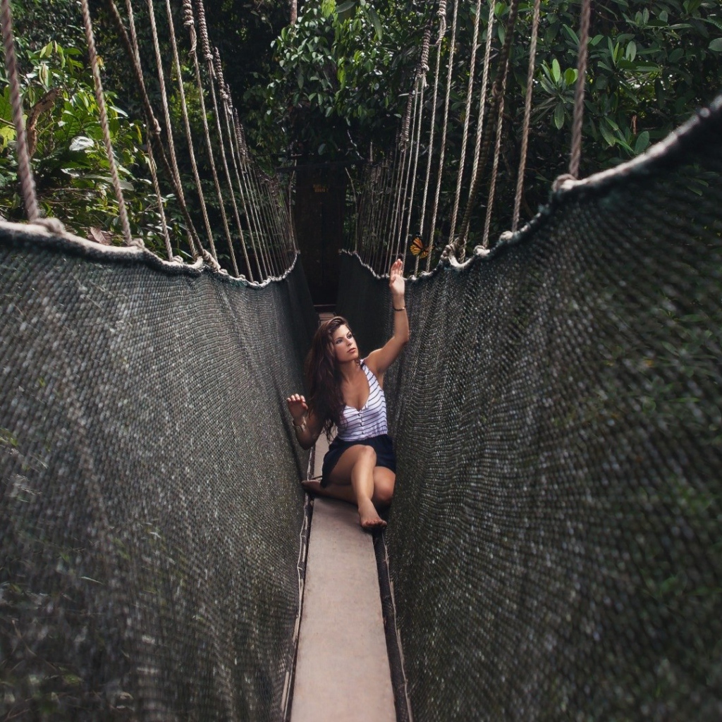 Девушка сидит на подвесном мосту