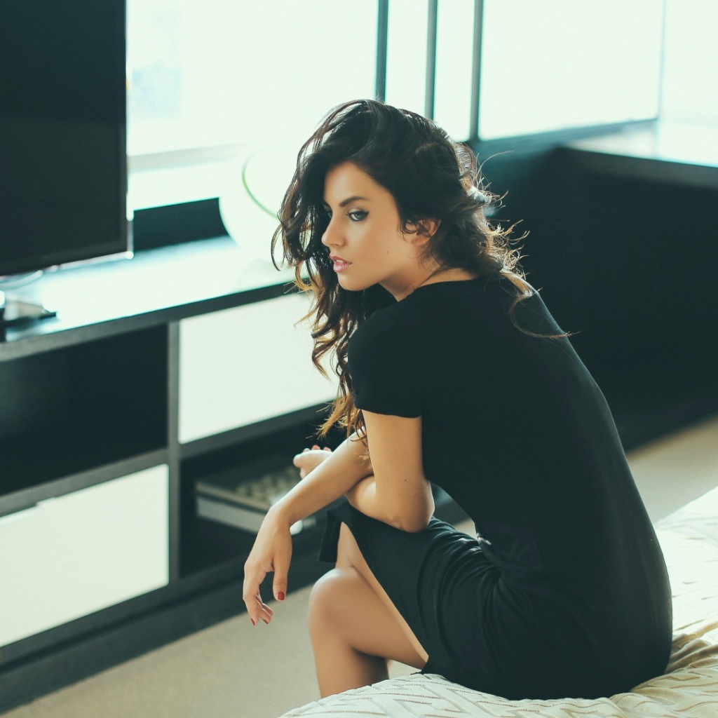 Девушка сидит на кровати перед телевизором