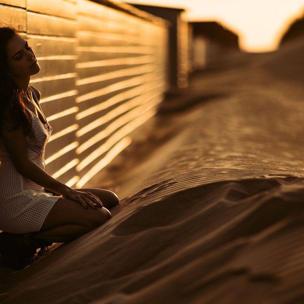 Girl sitting on the sand near the fence