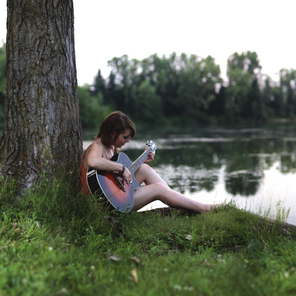Девушка сидит  с гитарой на берегу реки