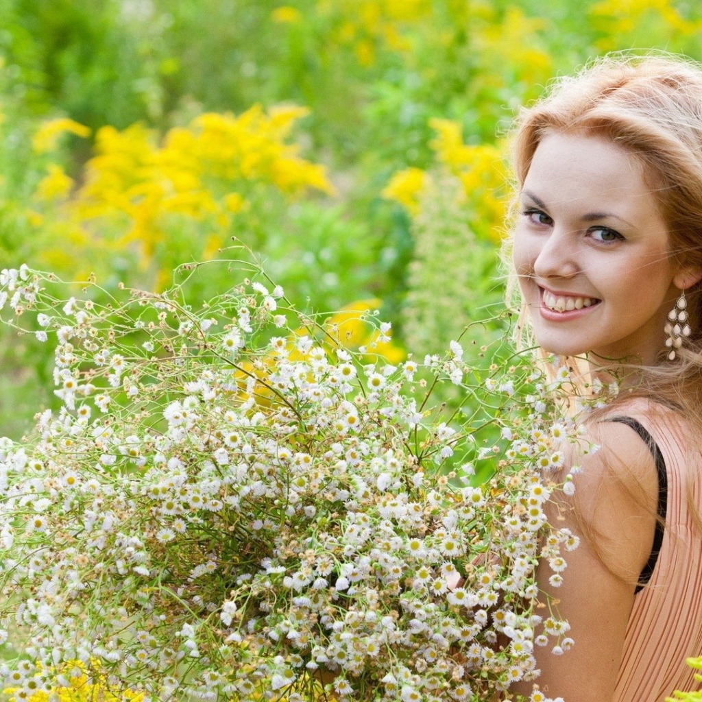Девушка улыбается, держа в руках букет ромашек