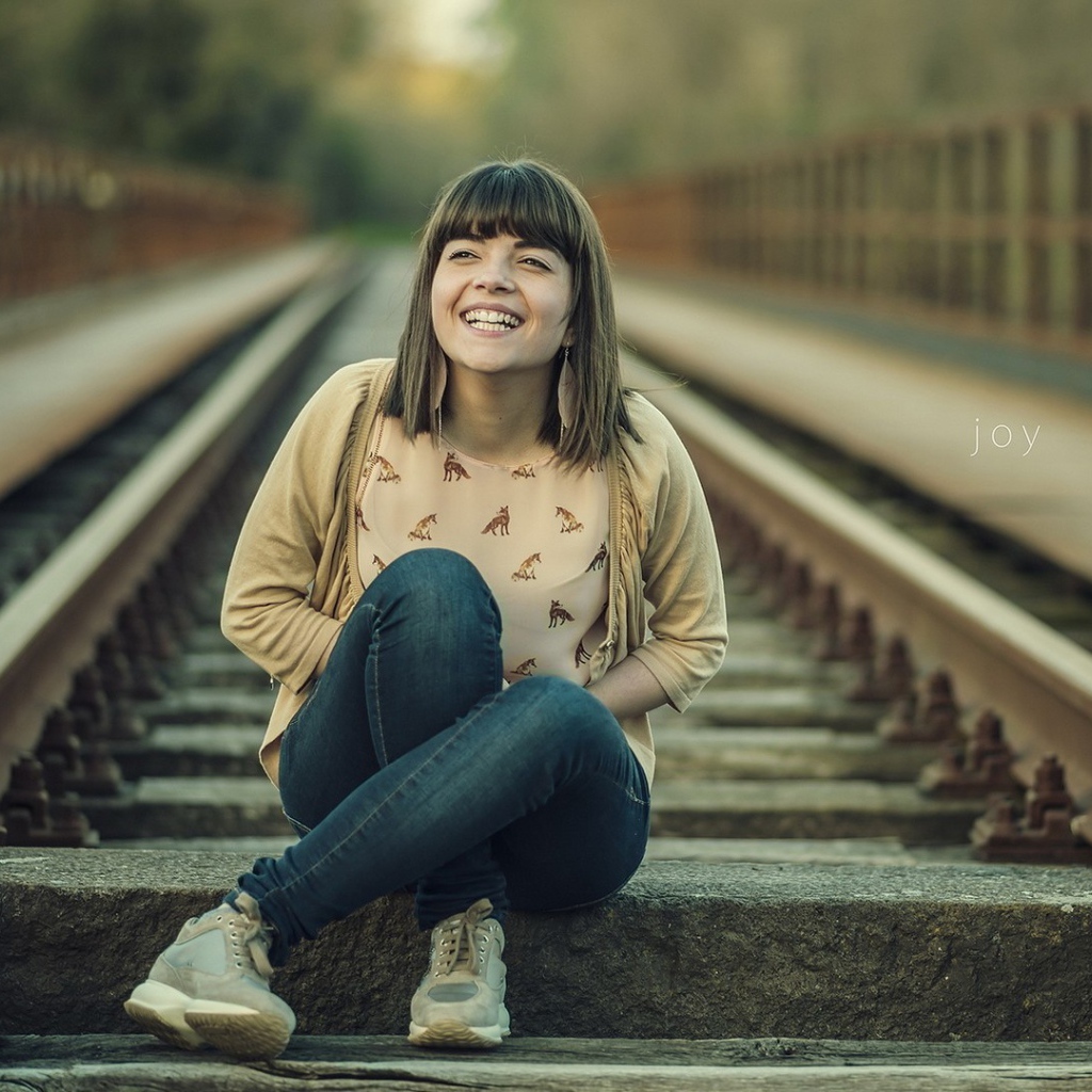 Девушка улыбается сидя на рельсах