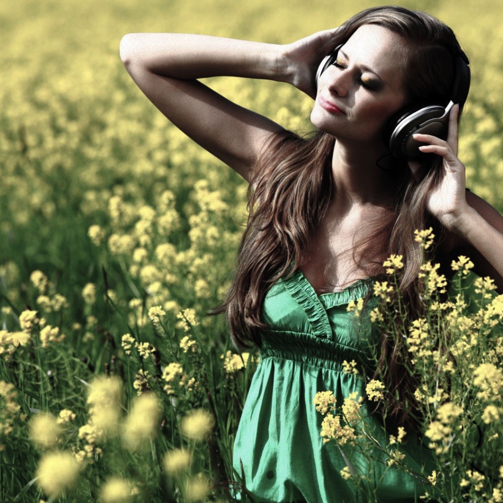 Девушка стоит среди цветов в наушниках