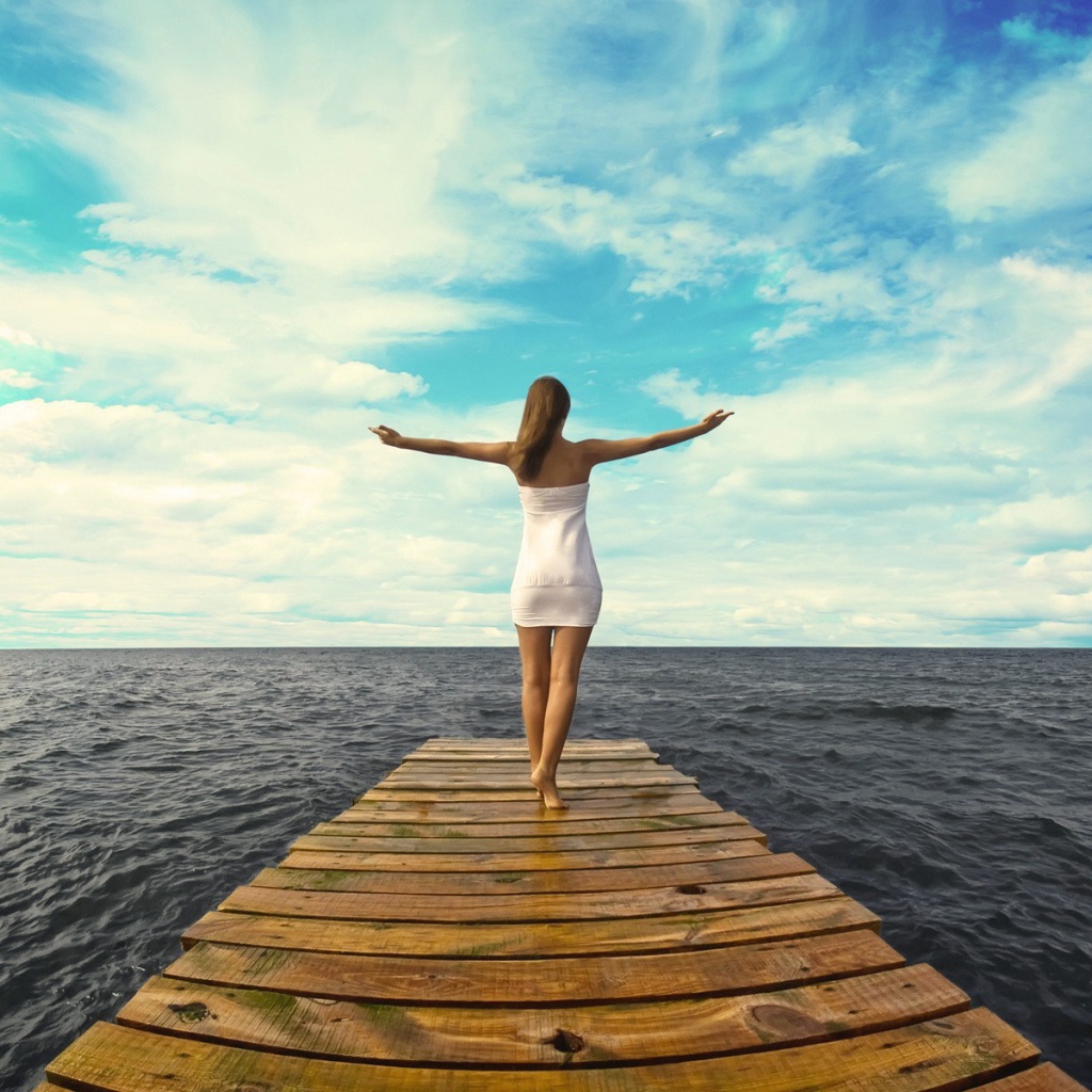 Девушка стоит раскинув руки на краю причала