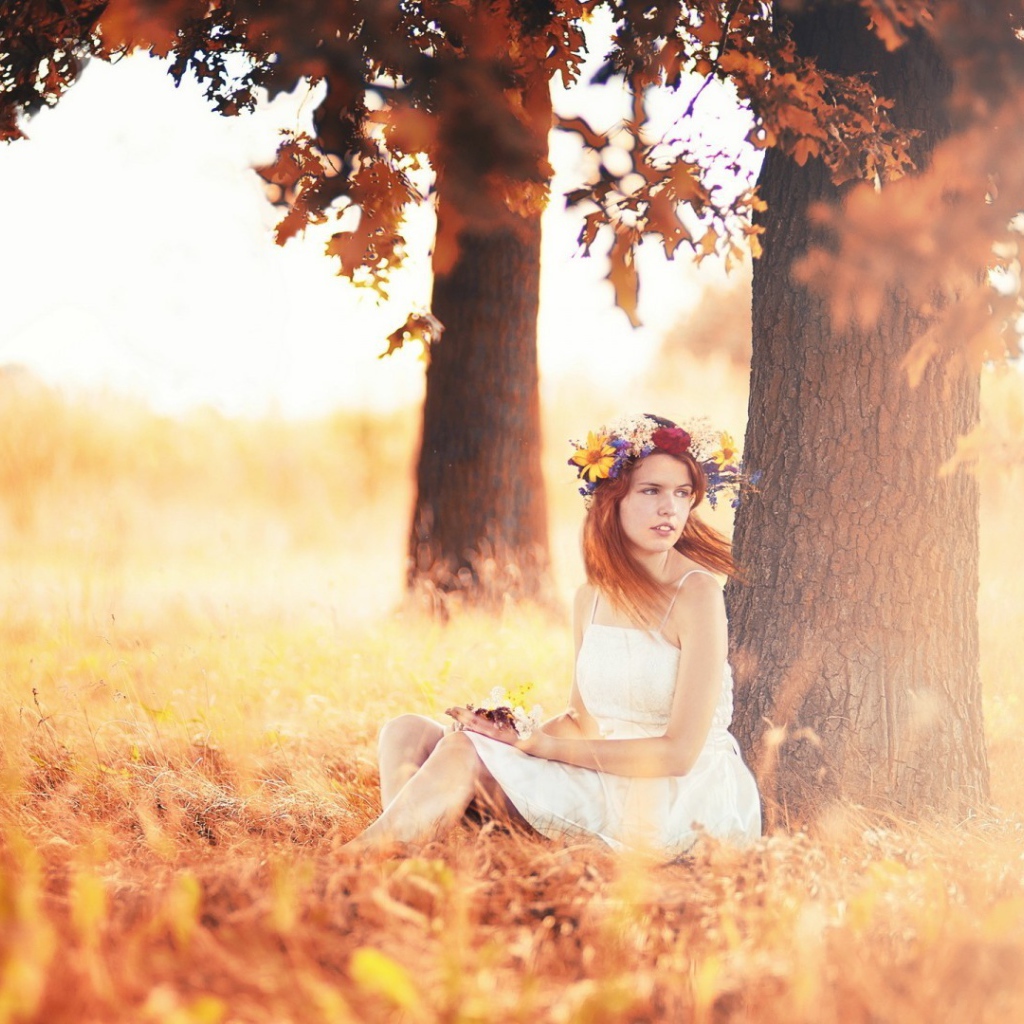 Девушка с венком на голове сидит под осенним деревом