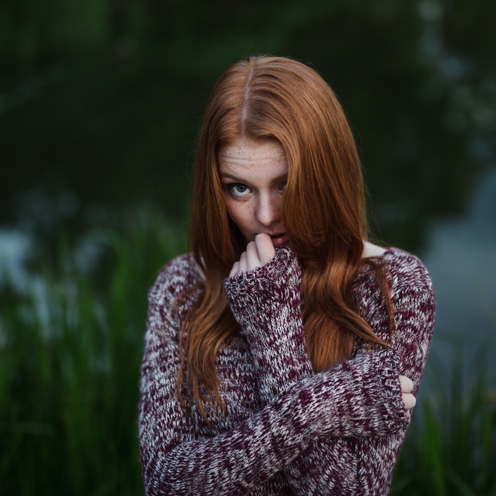 Рыжая девушка в свитере на фоне водоема