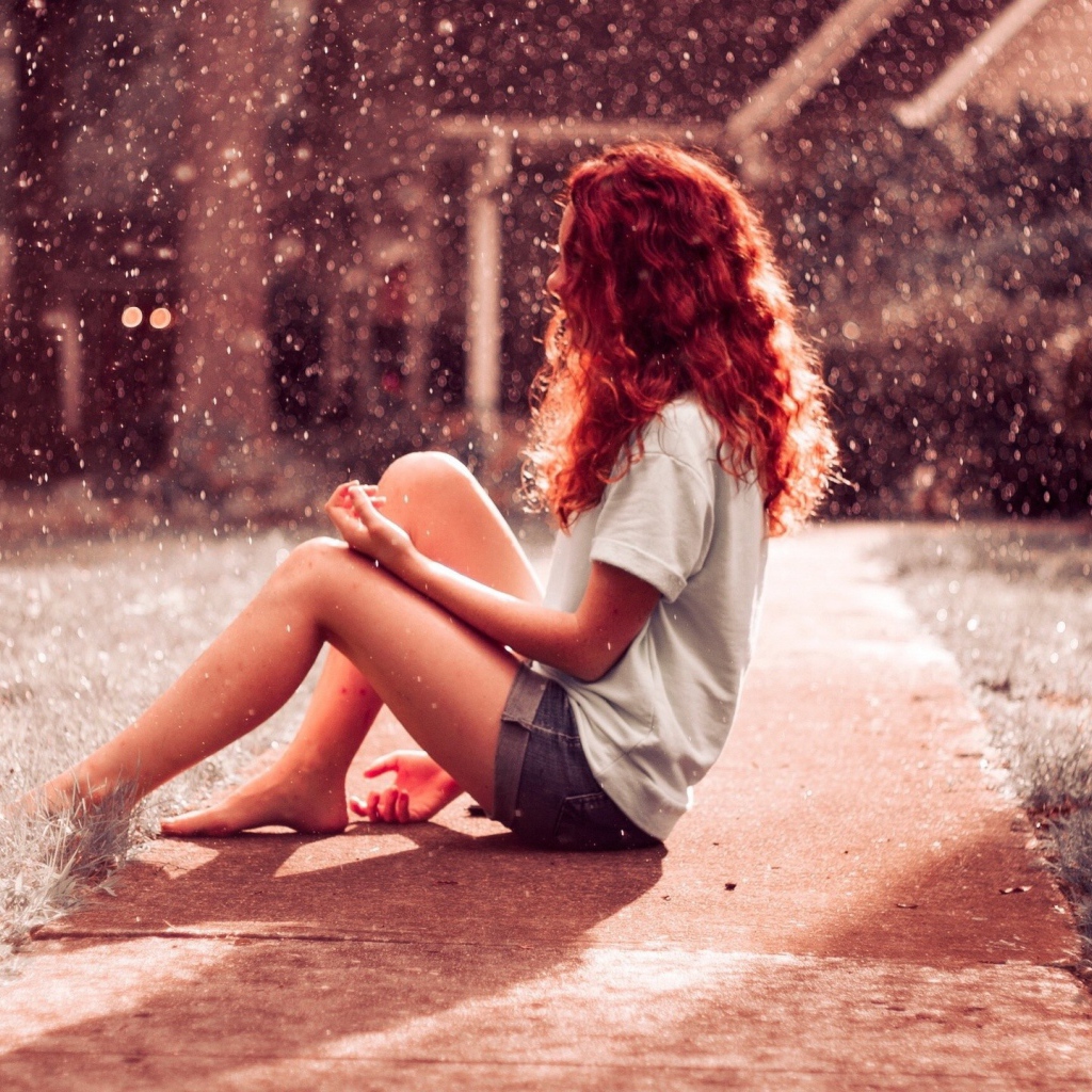 Рыжая девушка сидит на земле во время дождя