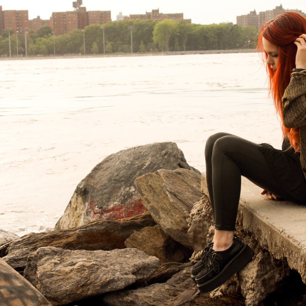 Рыжая девушка сидит на плитах набережной
