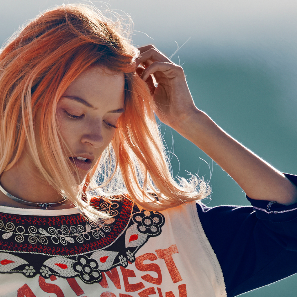 Рыжая девушка на ветру поправляет волосы
