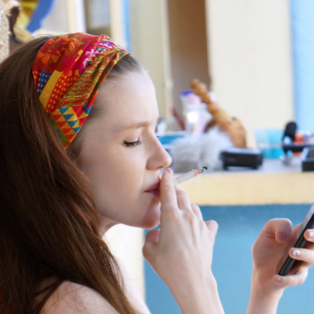 Девушка курит и смотрит на экран телефона