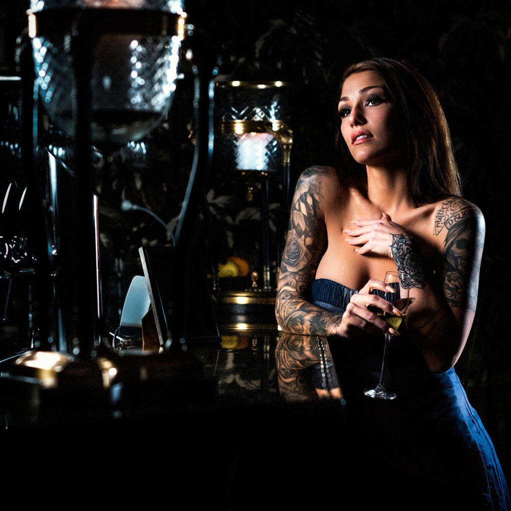 Татуированная девушка пьет вино в баре