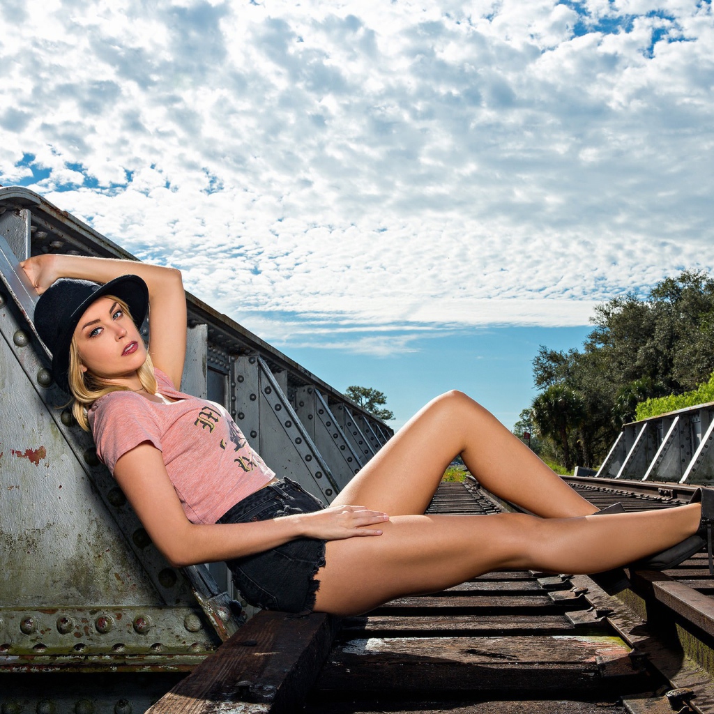 Блондинка в шляпе позирует на железной дороге