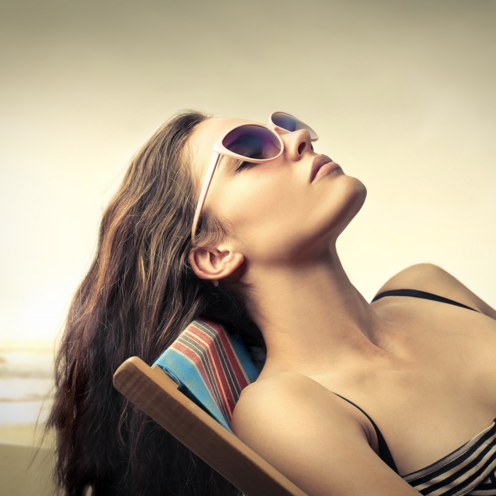 Девушка в очках загорает в шезлонге