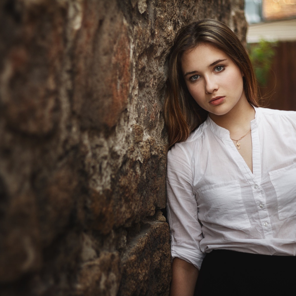 Девушка в белой рубашке стоит у стены