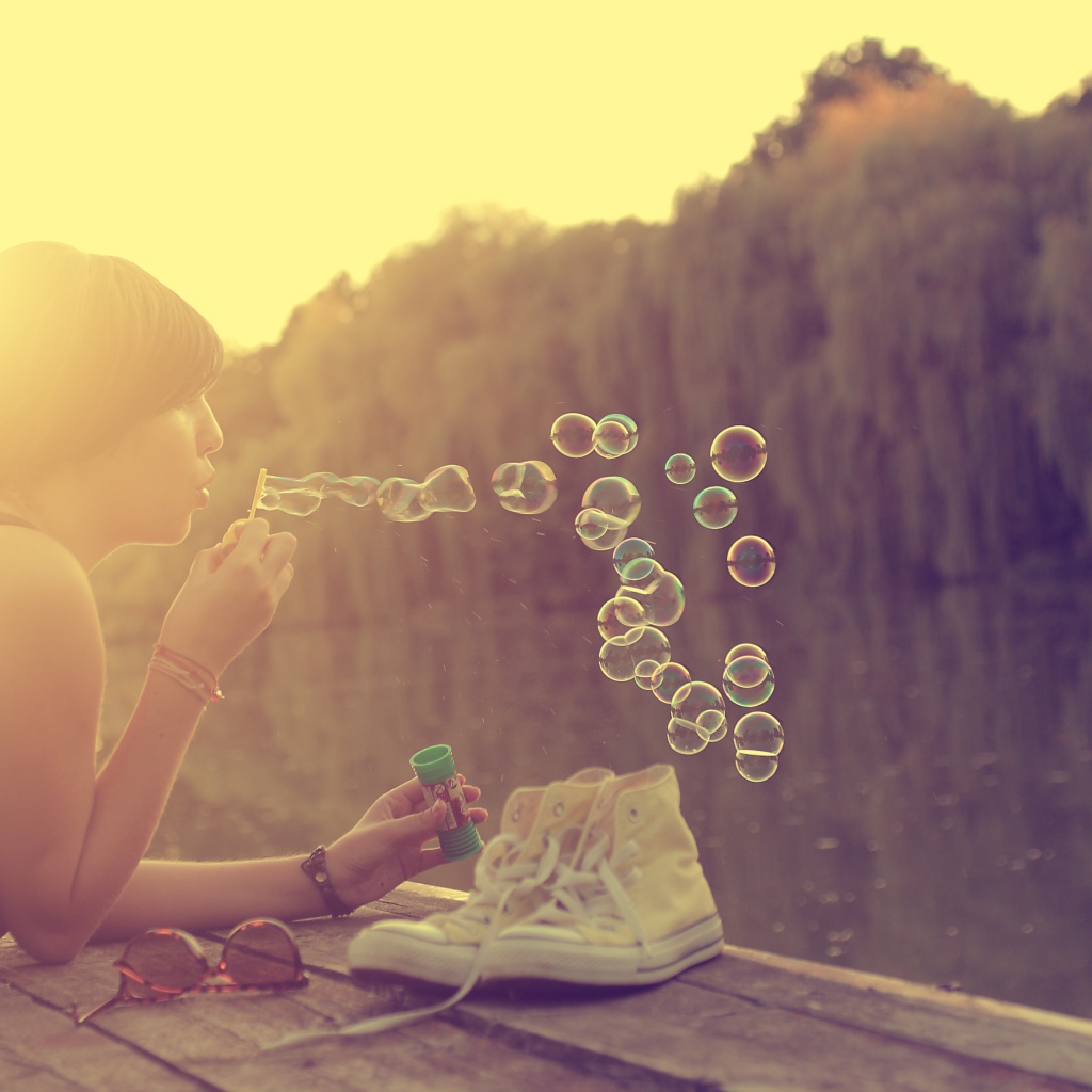 Девушка лежит на пирсе и играет с мыльными пузырями