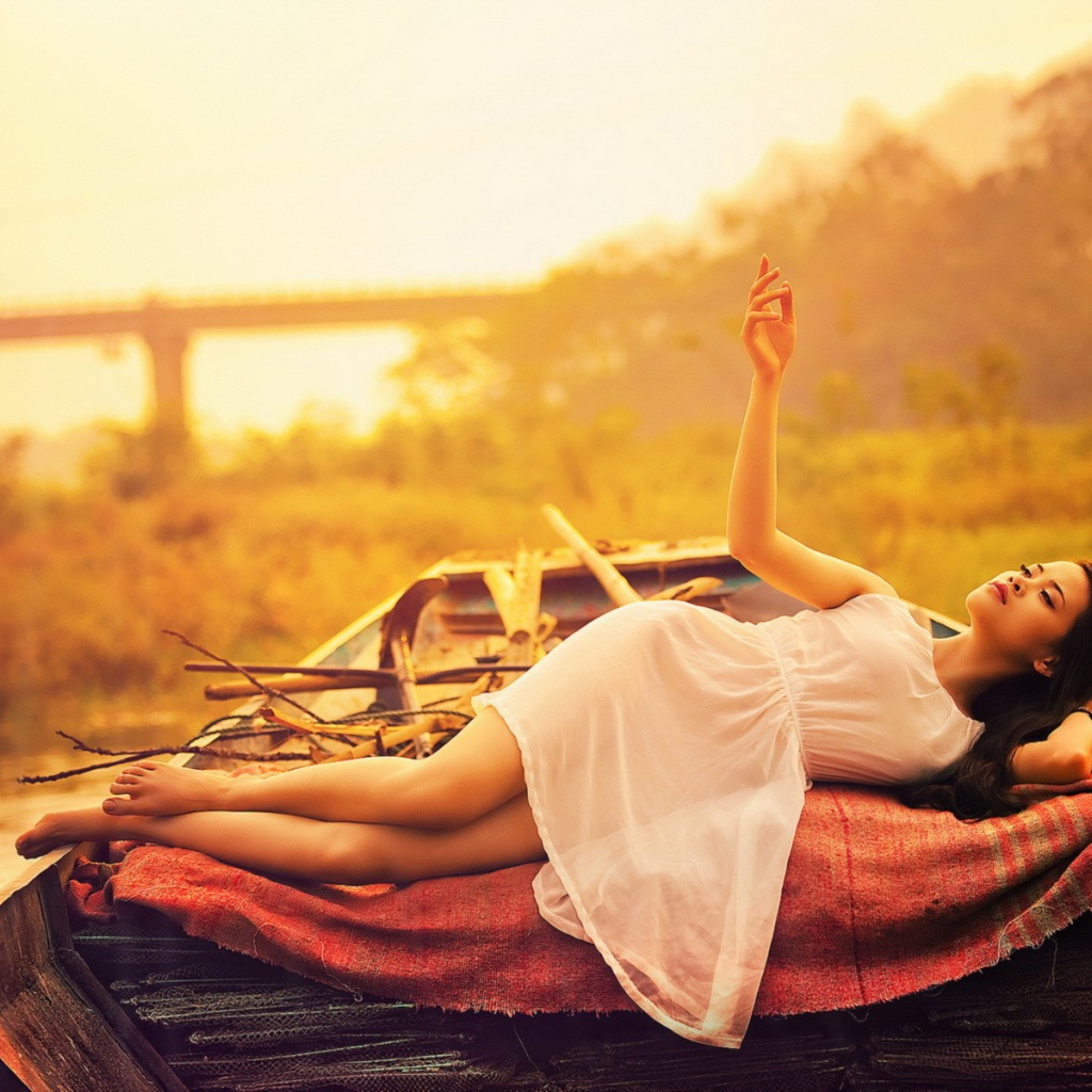 Азиатская модель в белом платье лежит в лодке