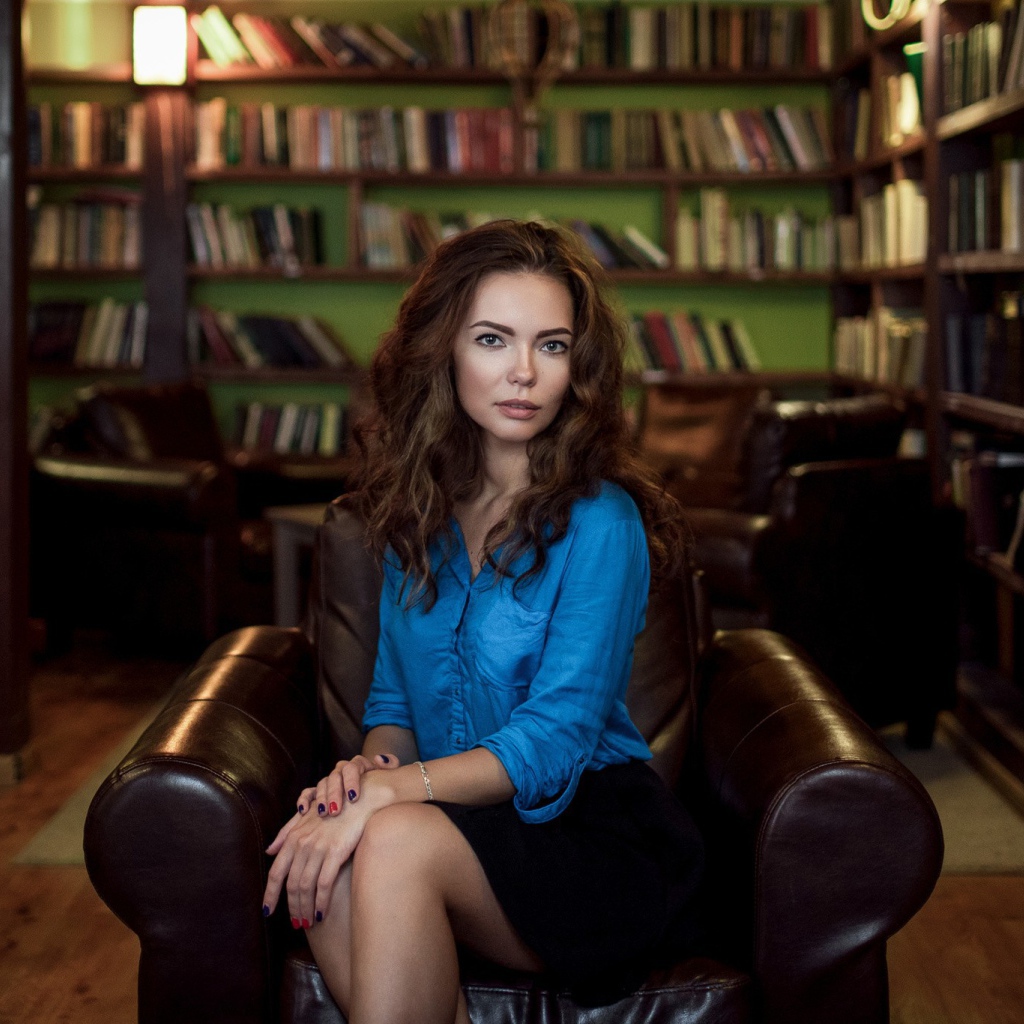 Модель в голубой блузке сидит на кожаном кресле