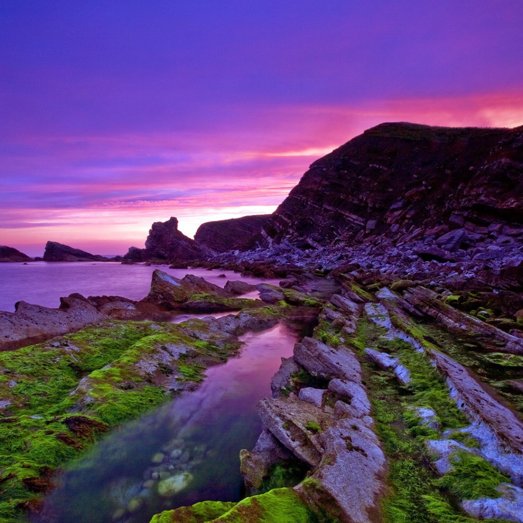 Голые скалы у берега на фоне сиреневого заката