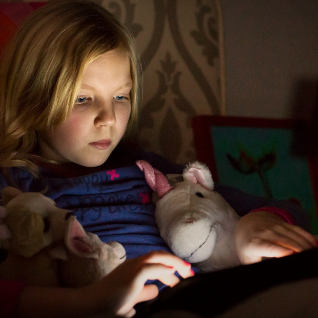 Девочка играет с планшетом лежа в кровати