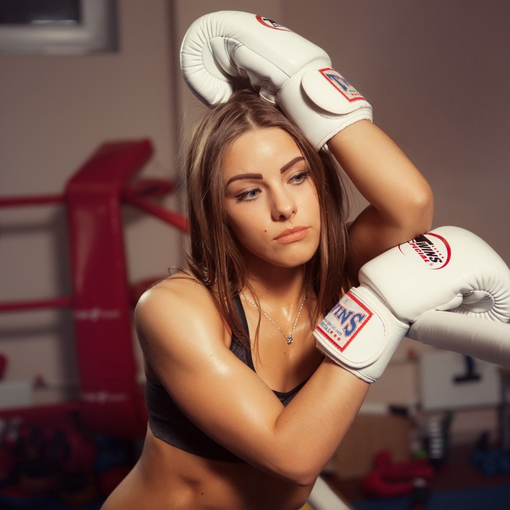 Девушка в белых перчатках отдыхает у канатов ринга